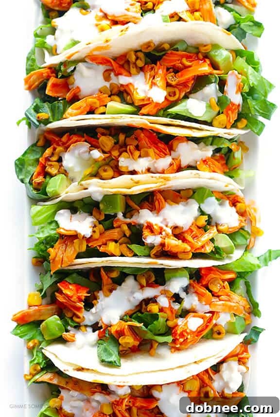 Several Buffalo Chicken Tacos garnished with fresh cilantro and green onions, served on a platter.