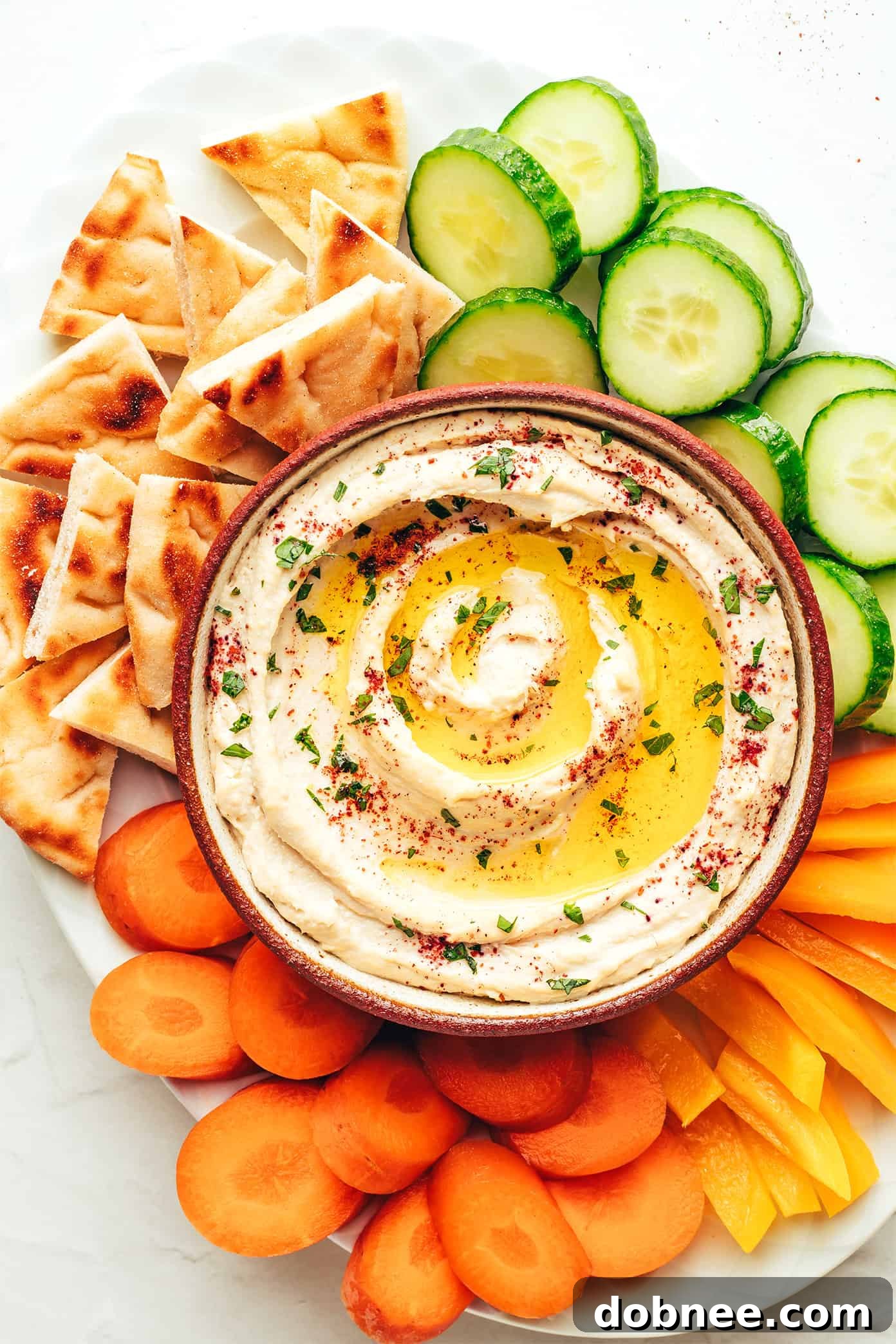 A beautifully plated bowl of homemade hummus, garnished with olive oil, herbs, and served with fresh pita bread.