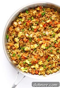 A vibrant bowl of Quinoa Fried 'Rice' with scrambled egg, green onions, and colorful vegetables.