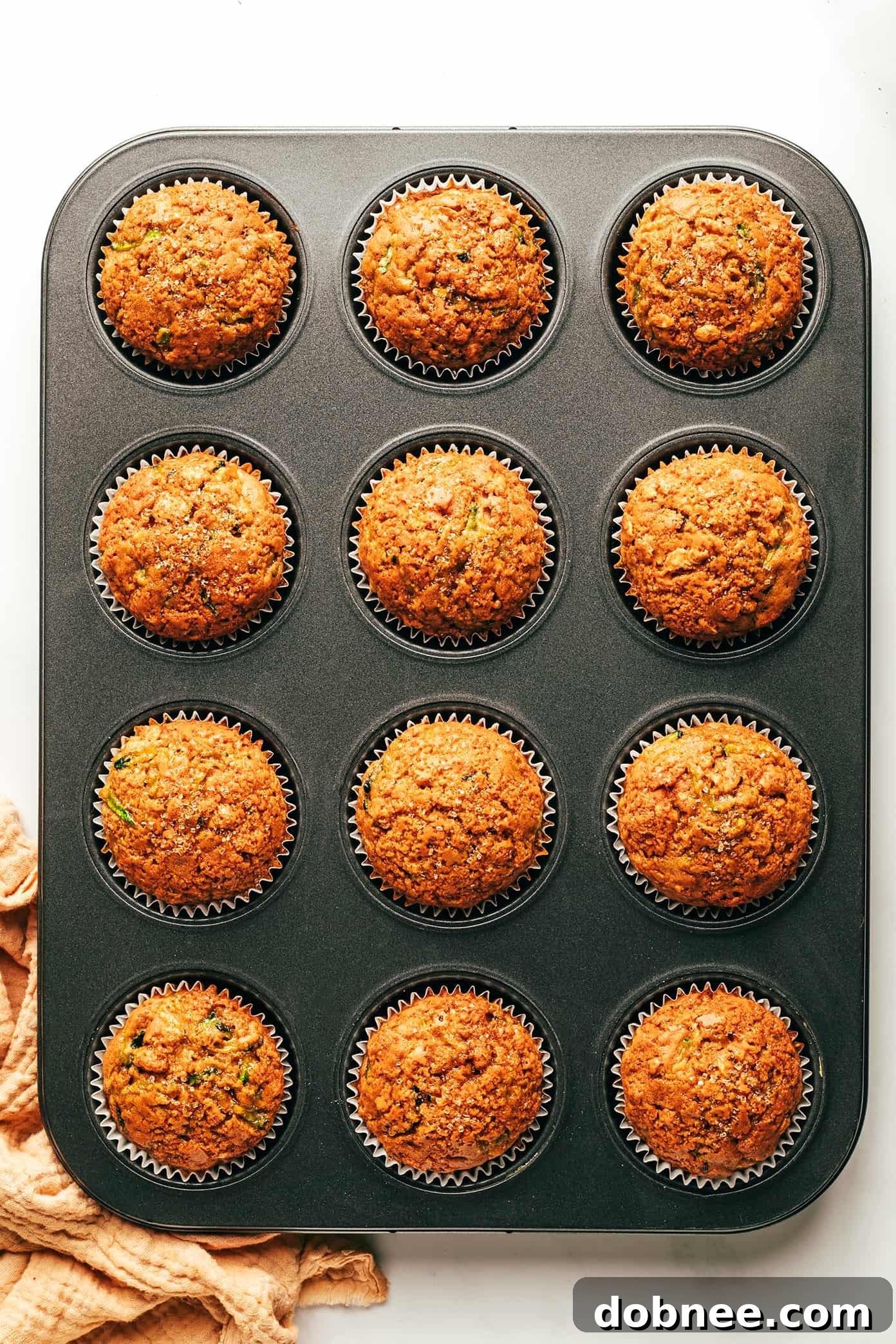 Two hands reaching for a freshly baked healthy zucchini muffin, emphasizing its inviting warmth.