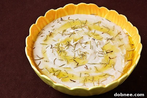 Exquisite Roasted Garlic, Rosemary, and White Bean Hummus served in a rustic bowl, garnished with fresh rosemary sprigs and a drizzle of olive oil, ready to be enjoyed.