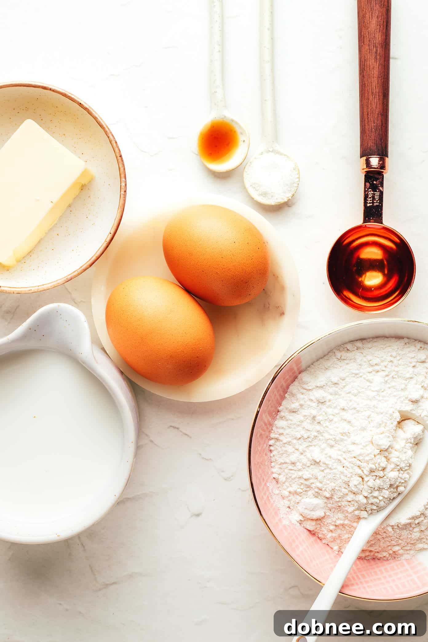 Seven basic ingredients for making classic French crepes laid out on a wooden surface.