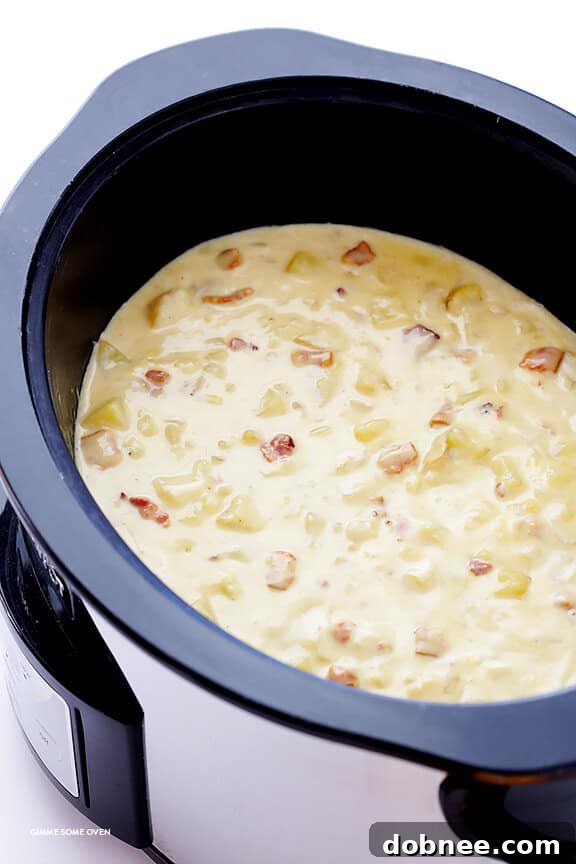 Potato masher being used to gently mash cooked potatoes in the slow cooker, adjusting the soup's thickness