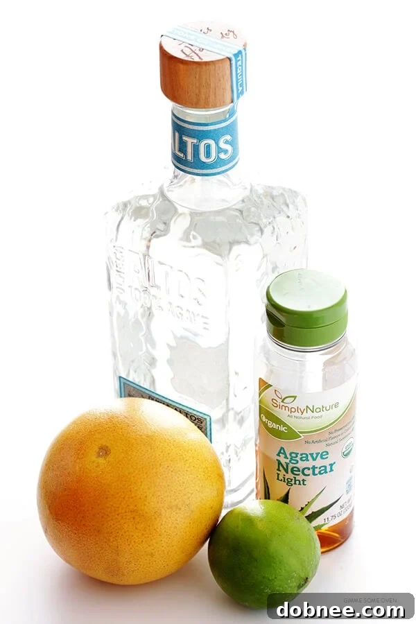 Ingredients laid out for making grapefruit margaritas, including fresh grapefruit, lime, tequila, and agave nectar