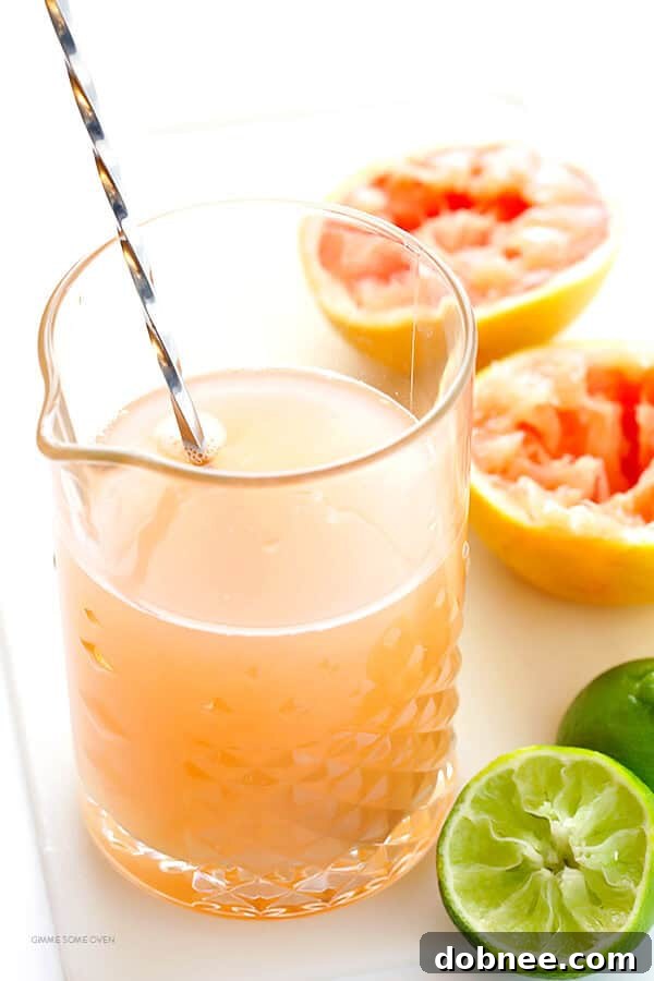 A hand squeezing fresh grapefruit juice into a measuring cup, demonstrating preparation for the cocktail