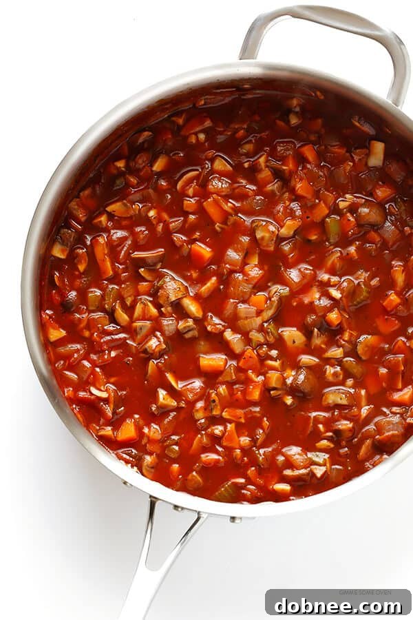 A large sauté pan overflowing with a vibrant mix of diced vegetables like carrots, celery, onions, and various mushrooms, ready to be simmered into a rich bolognese sauce.