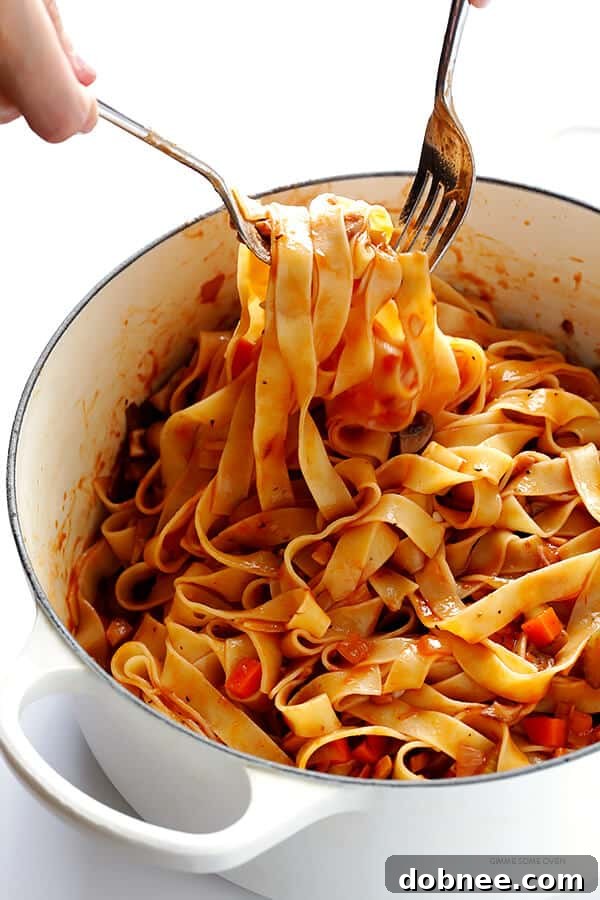 Cooked tagliatelle pasta being tossed directly with a rich, hearty mushroom bolognese sauce in a large pan.