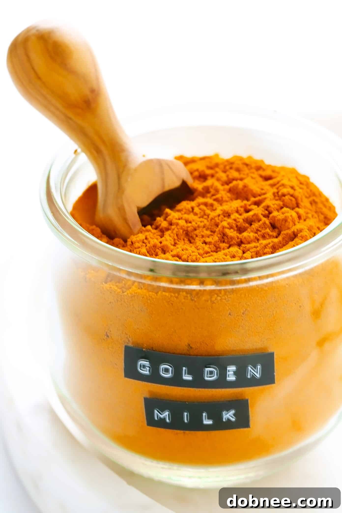A jar of homemade golden milk spice mix, labeled, on a wooden table.