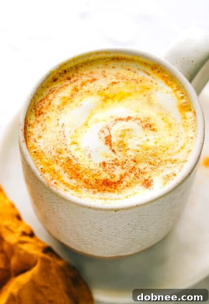 A glass of golden milk, hot or iced, with spices surrounding it.