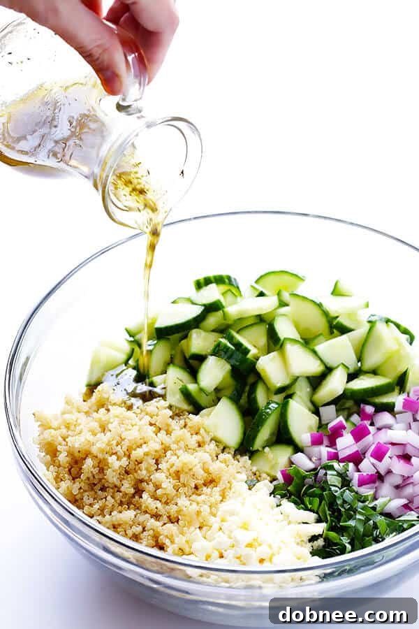 A simple yet vibrant lemon vinaigrette being drizzled over a bowl of cucumber, quinoa, feta, basil, and red onion.