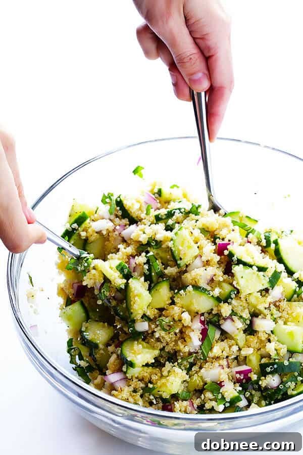 The Cucumber Quinoa Salad ingredients being gently tossed together with the lemon vinaigrette in a mixing bowl.