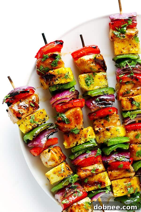 Hand threading chicken, bell peppers, pineapple, and red onion onto a skewer in a rainbow pattern.