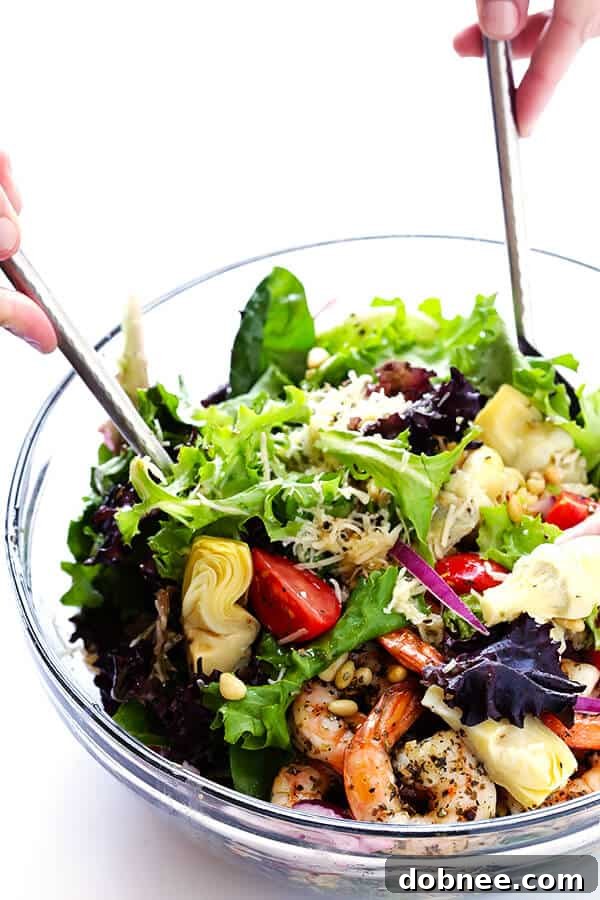 Tossing the Shrimp and Artichoke Green Salad with the lemon vinaigrette to ensure all ingredients—shrimp, artichokes, tomatoes, pine nuts, and greens—are evenly coated and perfectly seasoned for maximum flavor. The ultimate fresh and savory salad experience.