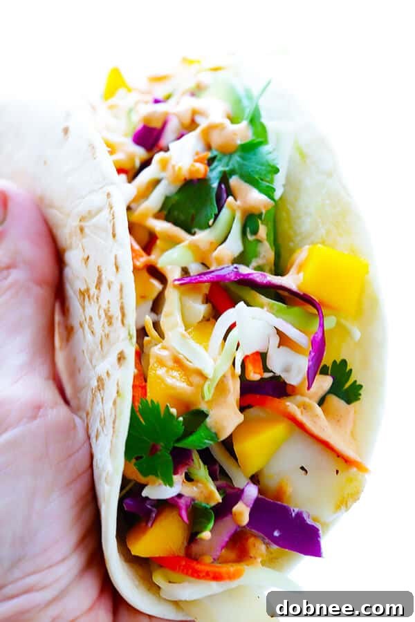 Assembled mango chipotle fish taco, bursting with fresh ingredients and drizzled with creamy sauce.