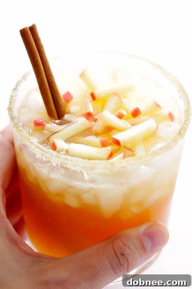 An exquisite Smoky Apple Cider Mezcal Margarita, perfectly garnished with a cinnamon stick and fresh apple slices, ready to be enjoyed as the ideal autumn refreshment.