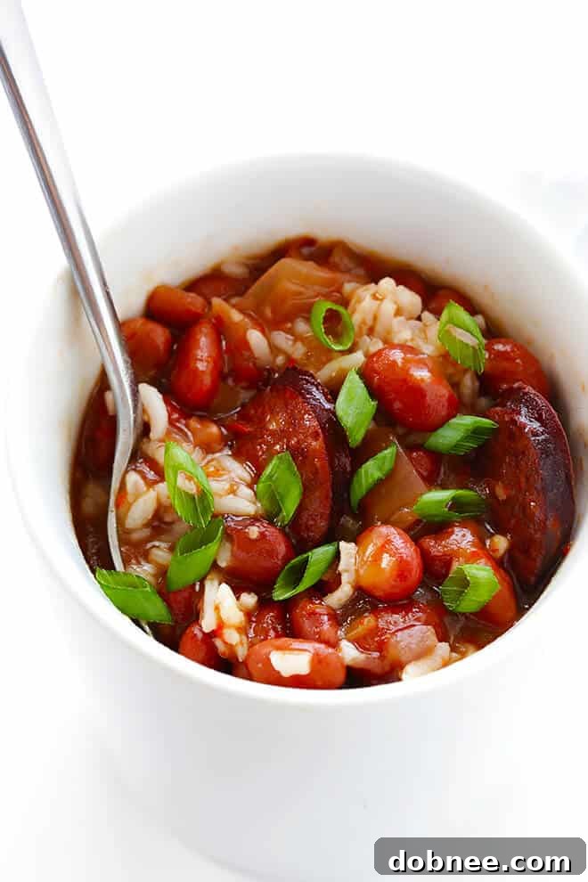 A top-down view of the entire slow cooker filled with Red Beans and Rice, garnished with green onions and a spoon, ready for serving.