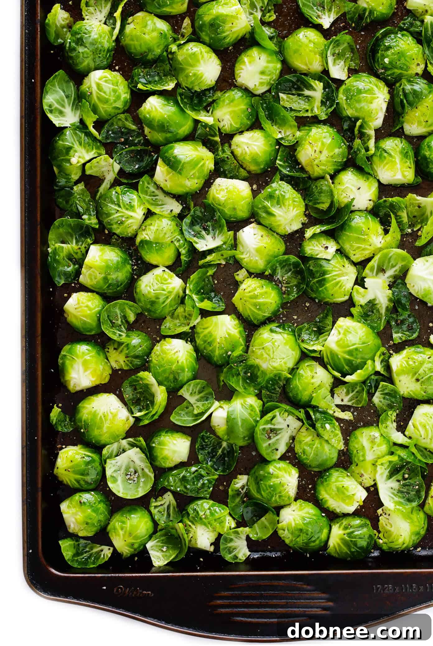 A close-up of Brussels sprouts being trimmed and halved on a cutting board, demonstrating the preparation process for roasting.