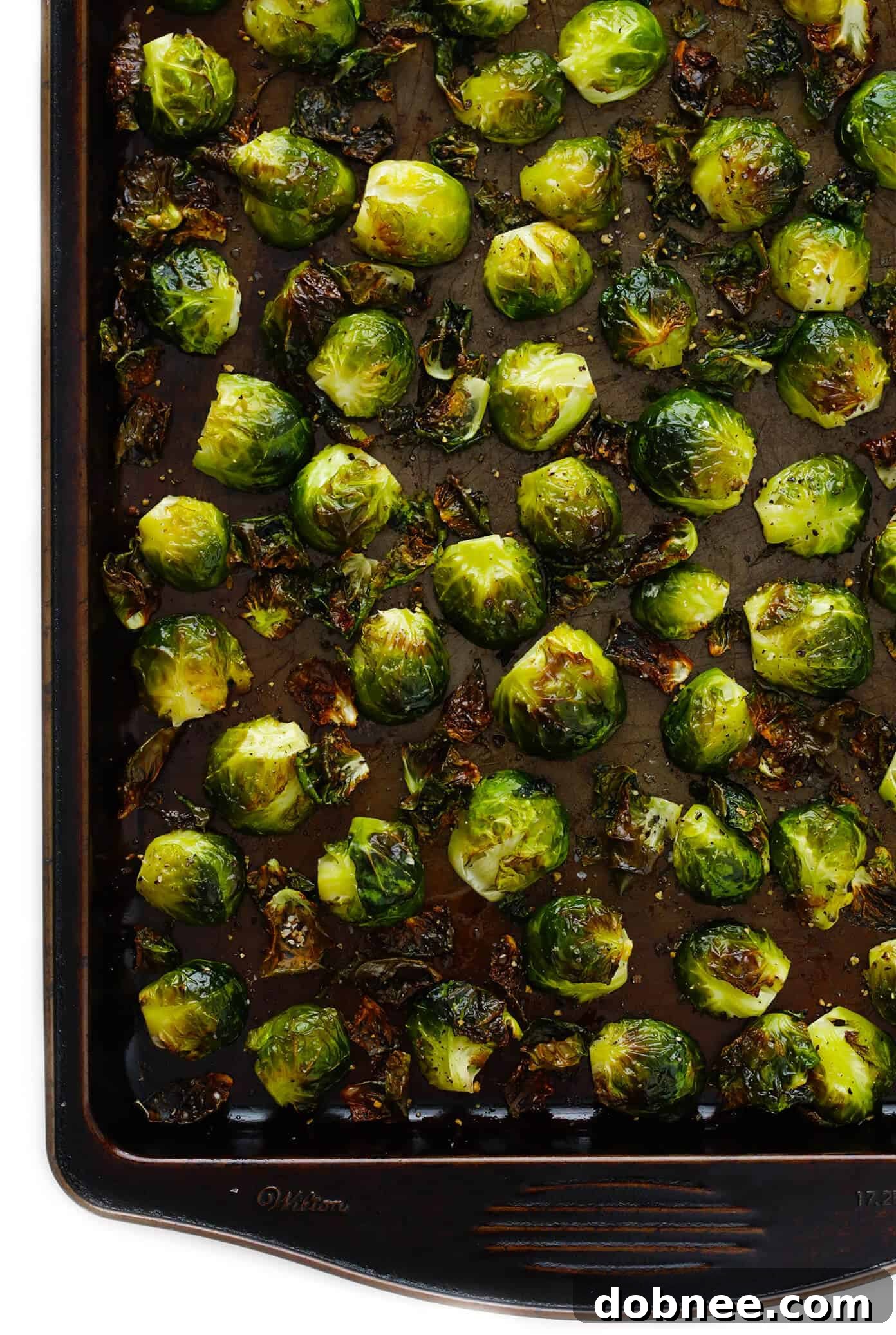 Halved Brussels sprouts tossed with olive oil, salt, and pepper on a baking sheet, ready for the oven.