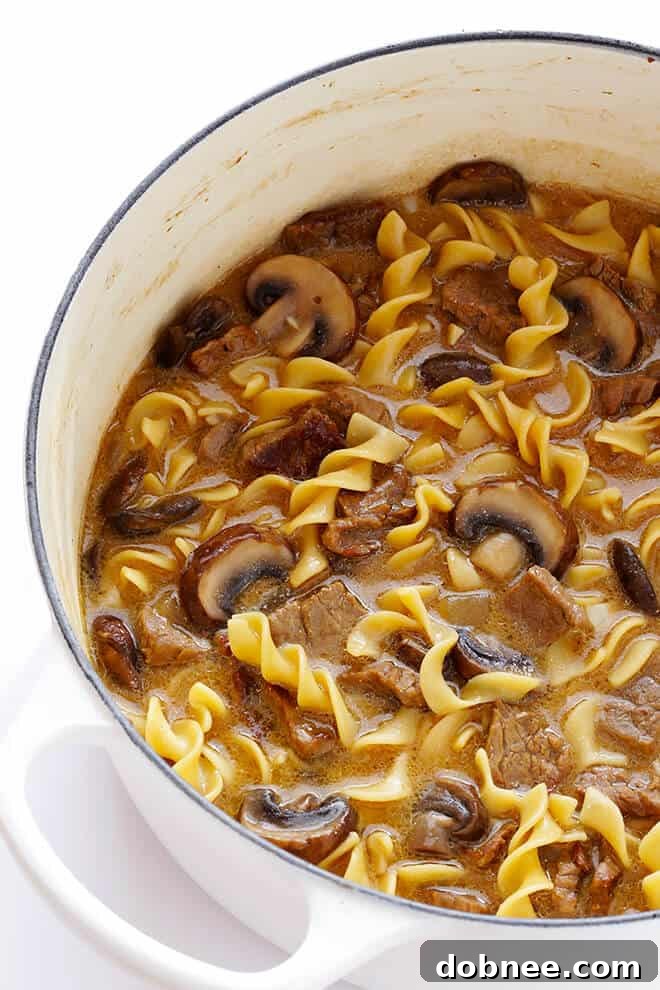 Close-up of fresh baby bella (crimini) mushrooms, onions, and garlic sautéing in a pan for Beef Stroganoff Soup, building essential flavor layers.