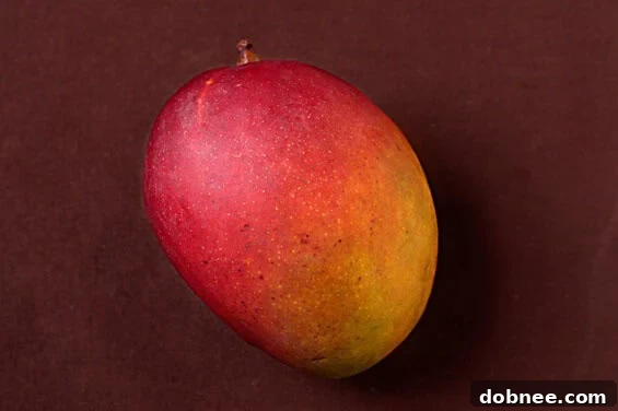 Hands gently squeezing a mango to check for ripeness, with a basket of mangoes in the background.