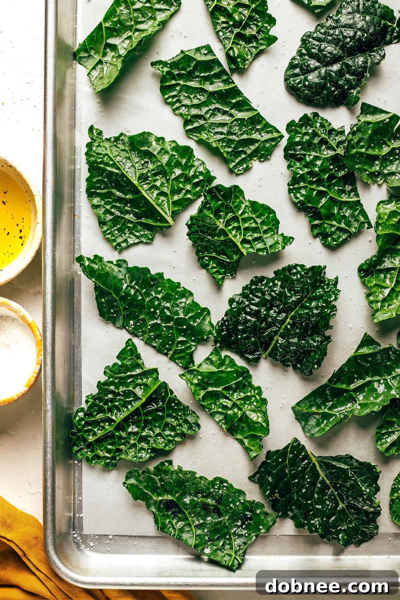 A close-up shot of kale leaves being drizzled with high-quality olive oil and sprinkled with fine sea salt, emphasizing the simple preparation steps.