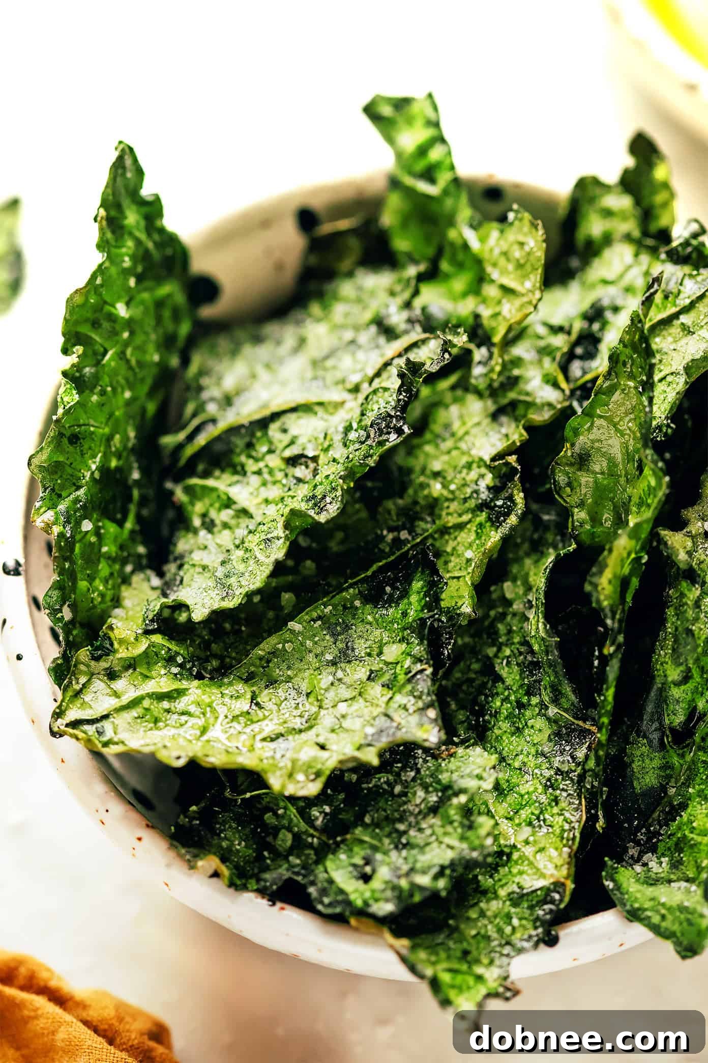 A close-up of a hand reaching for a perfectly seasoned, golden-brown kale chip from a rustic wooden bowl, emphasizing its enticing crisp texture.