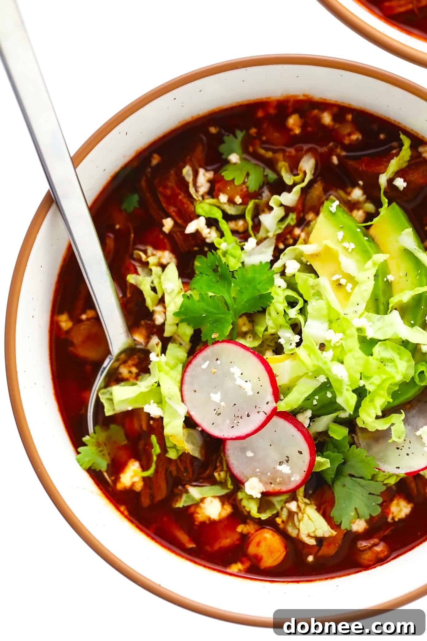 A vibrant bowl of Pozole Rojo generously topped with creamy avocado slices, crisp radishes, fresh cilantro, and shredded cabbage, ready to be enjoyed