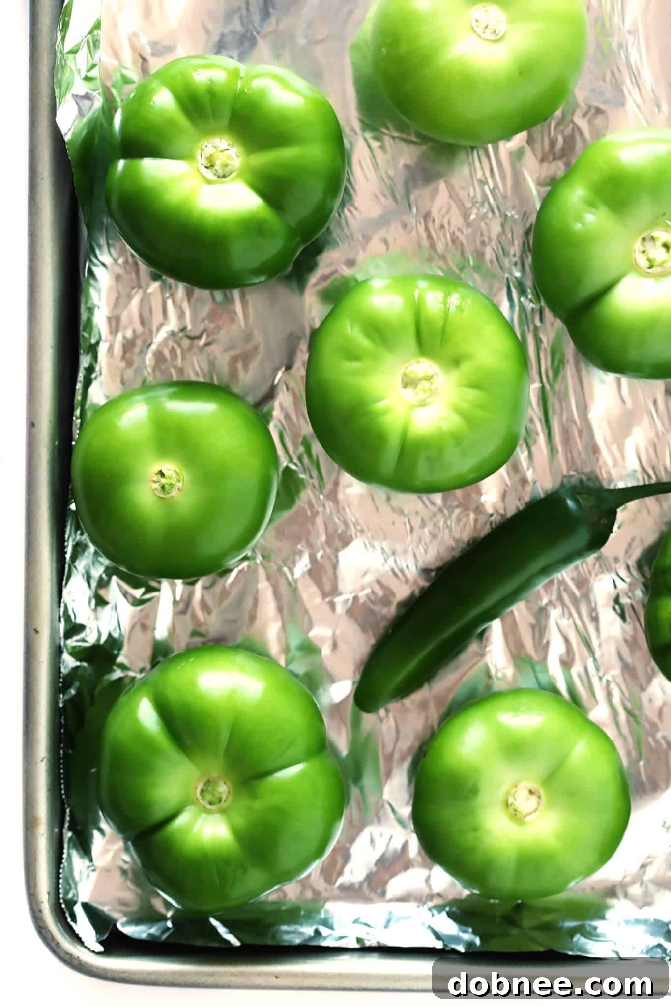 Close-up of roasted tomatillos, serrano peppers, and garlic cloves on a baking sheet, showcasing the perfect char for the best salsa verde recipe.