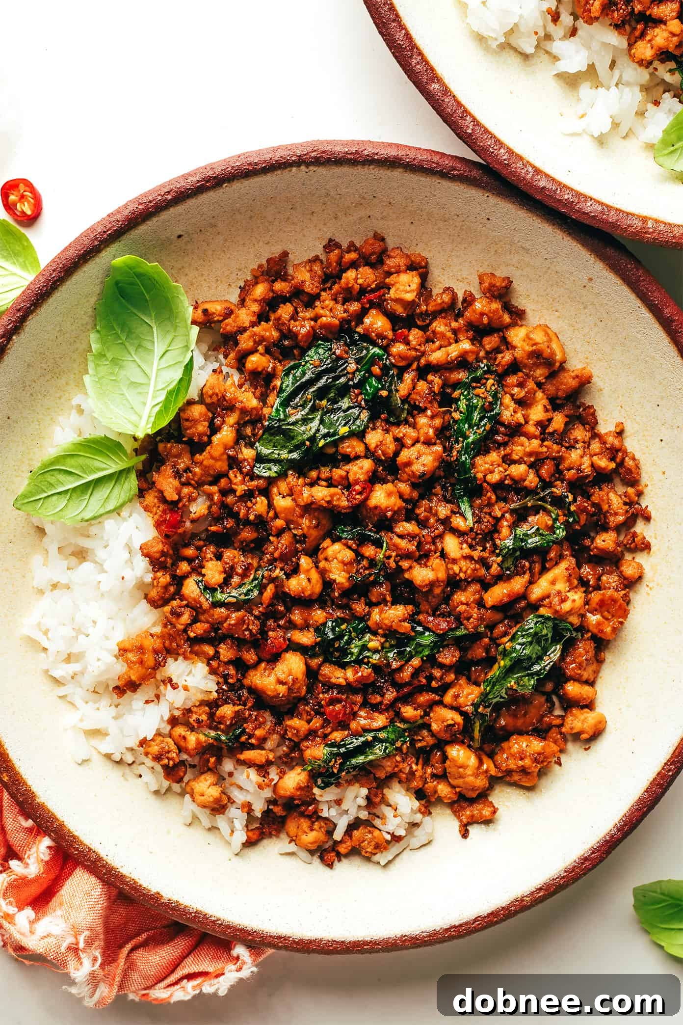 A vibrant close-up of freshly prepared Thai Basil Chicken (Gai Pad Krapow) served with steamed jasmine rice, garnished with fresh basil leaves and a lime wedge. The chicken is cooked to a perfect golden brown, mixed with colorful bell peppers and green beans.