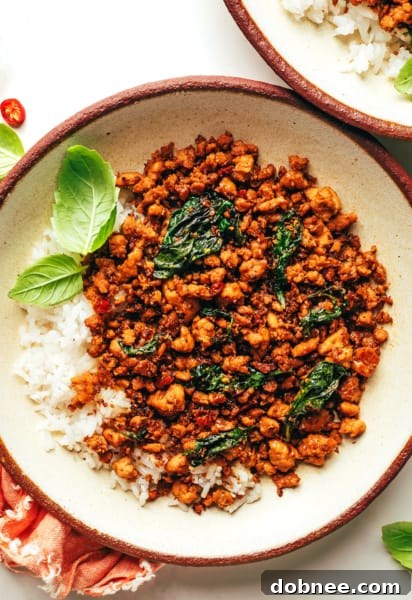 A vibrant plate of Thai Basil Chicken (Gai Pad Krapow) served with fluffy white rice, garnished with fresh basil leaves, ready to be enjoyed.
