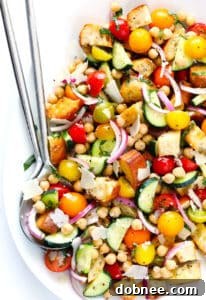 A vibrant Summer Panzanella salad in a large white bowl, featuring toasted bread, cherry tomatoes, cucumbers, chickpeas, and fresh basil.