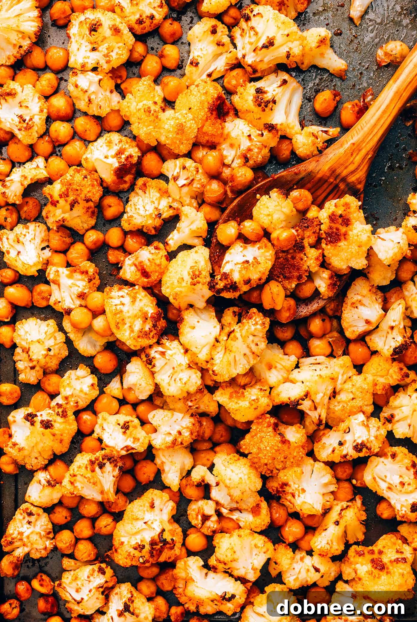 Hand drizzling creamy tahini dressing over a fresh roasted cauliflower and chickpea salad