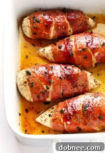 Prosciutto-Wrapped Baked Chicken Saltimbocca on a baking sheet, with a lemon wedge and fresh sage sprigs.