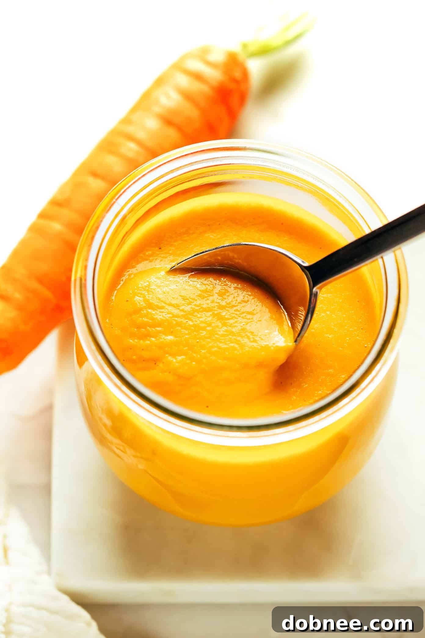 Bright orange carrot ginger dressing in a glass jar, next to fresh carrots and ginger