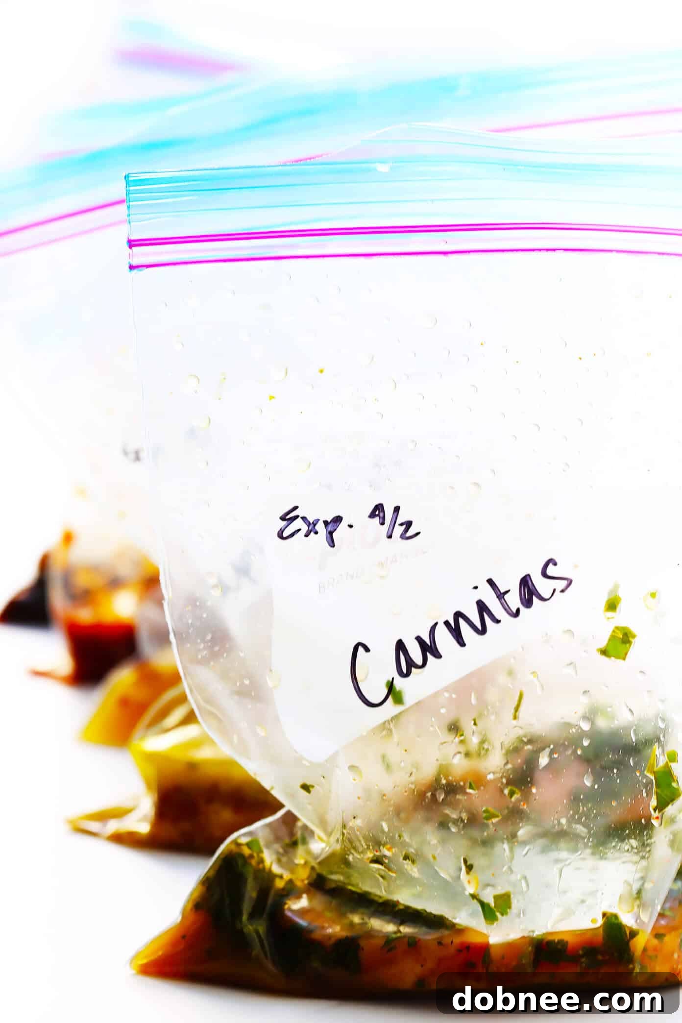 A close-up shot of a hand pouring a vibrant marinade into a freezer-friendly ziplock bag containing raw pork chops. The background shows other prepared marinade ingredients and a small bowl, emphasizing the ease of preparation and the meal prep aspect of the recipes.