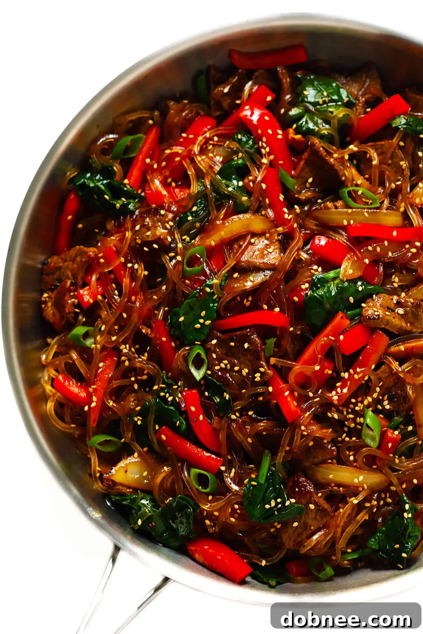 A step-by-step visual of the Japchae cooking process, showing a pan with stir-frying vegetables and noodles being mixed with the sauce.