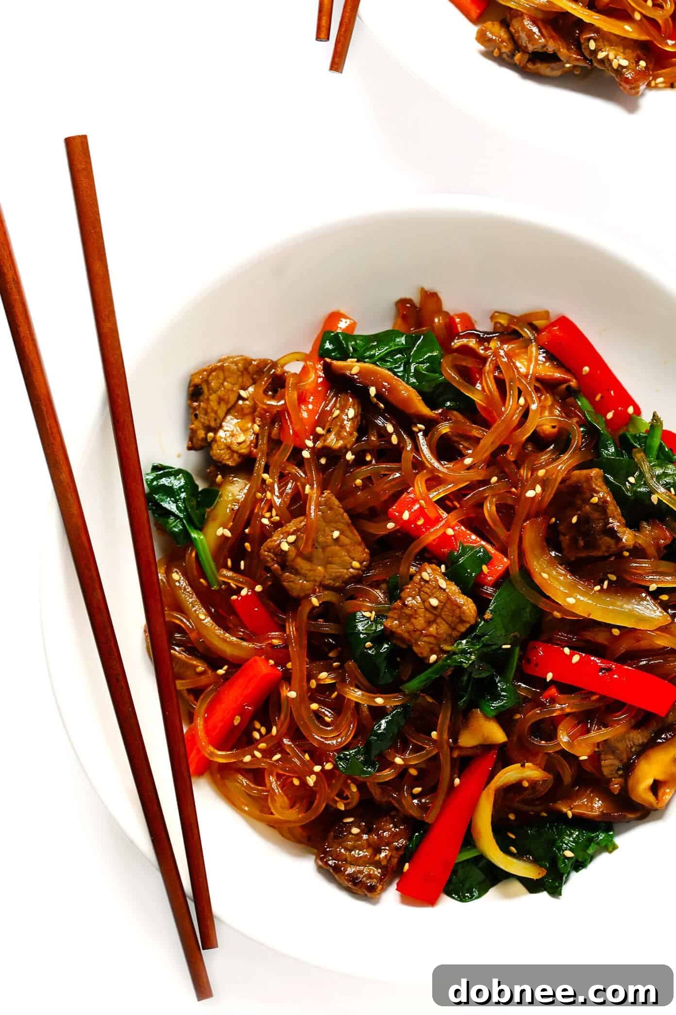 Japchae served in a bowl, highlighting the combination of beef, colorful vegetables, and the signature glass noodles. Garnished with sesame seeds.