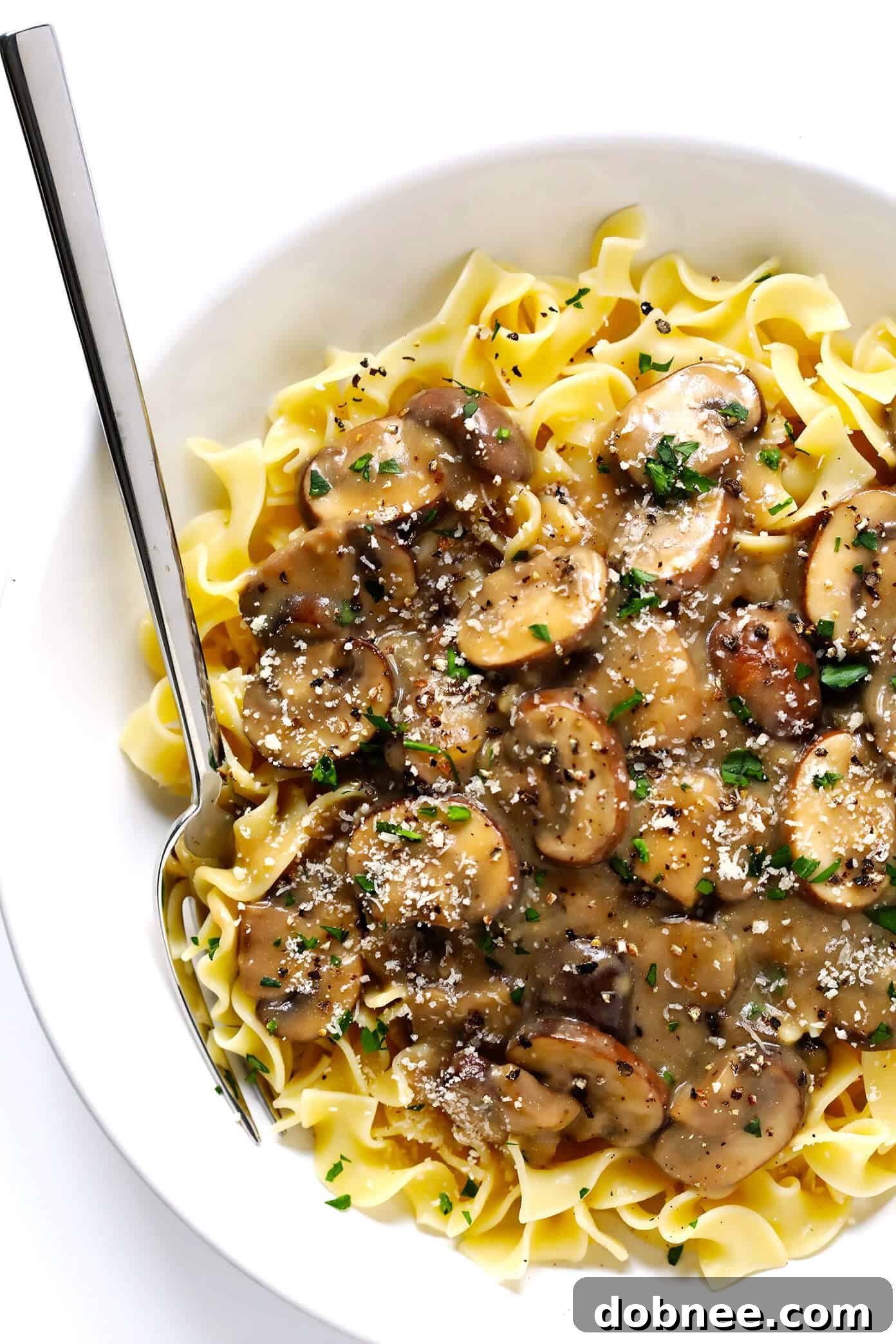 A chef's hands demonstrating how to combine vegetarian mushroom stroganoff sauce with egg noodles in a pan.
