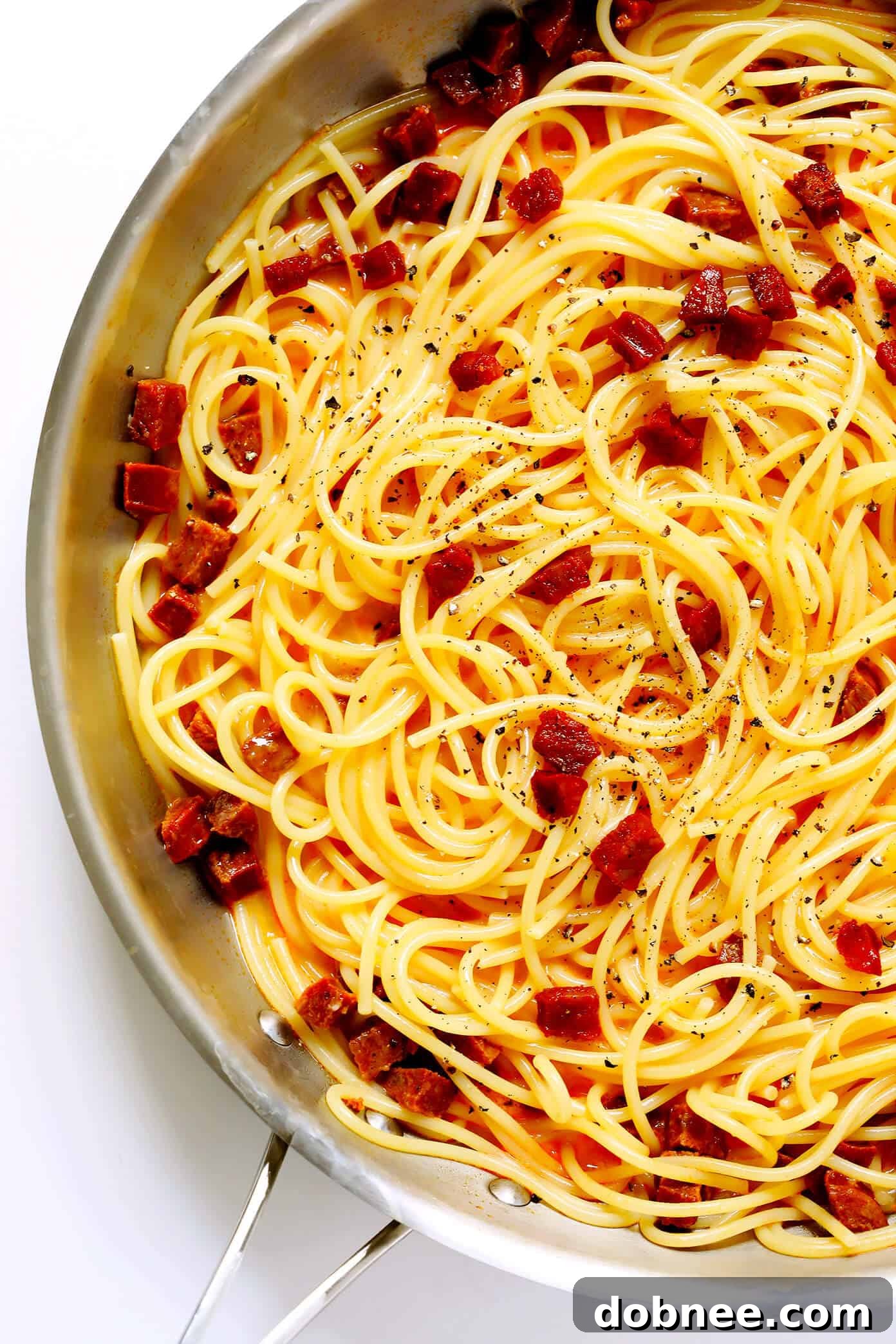 Freshly cooked spaghetti being tossed with crispy Spanish chorizo, creating a flavorful base for carbonara