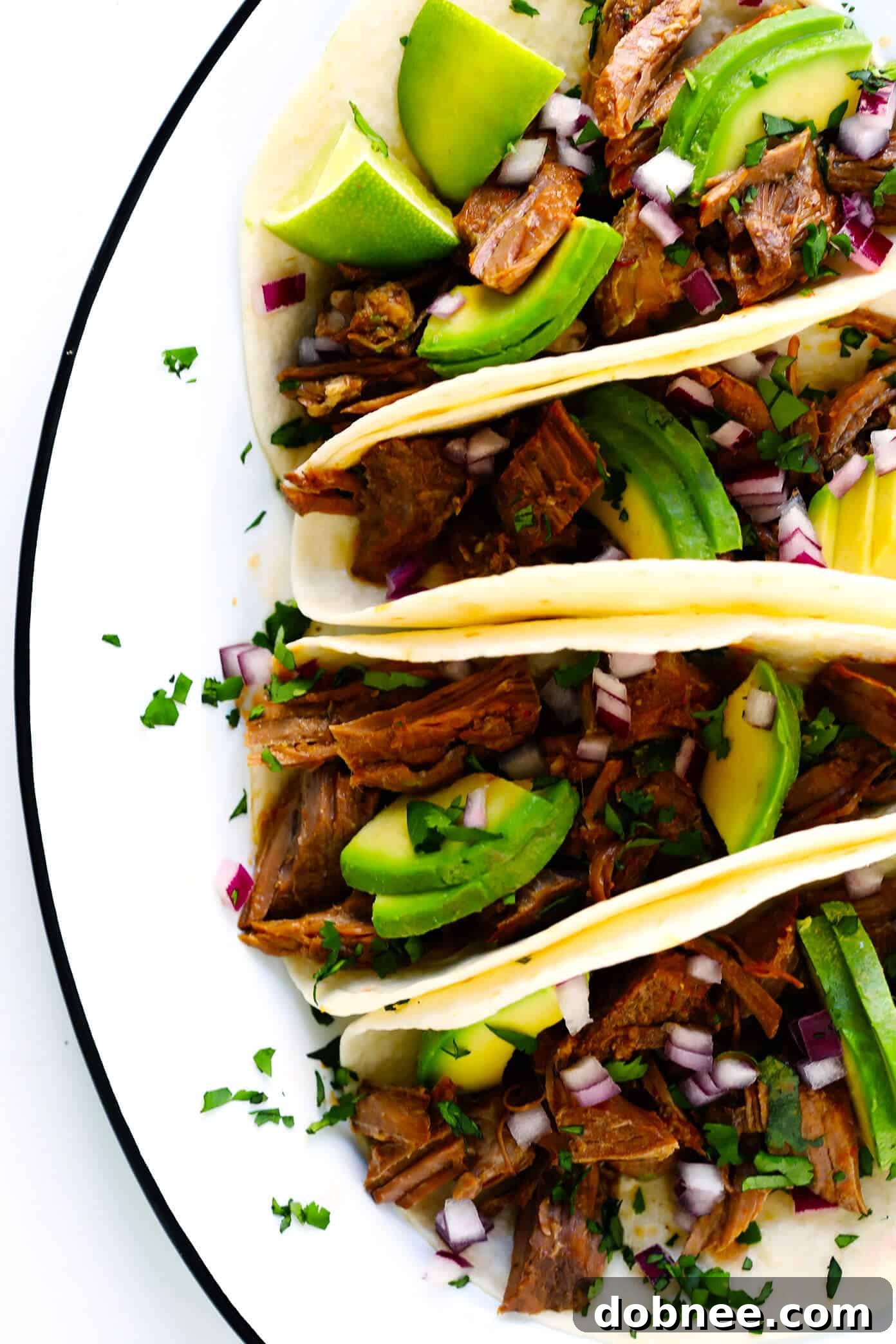 Serve this easy and delicious Instant Pot Barbacoa Beef in tacos with fresh avocado. A fantastic recipe for any occasion! Instant Pot Barbacoa Beef Tacos garnished with avocado, cilantro, and red onion