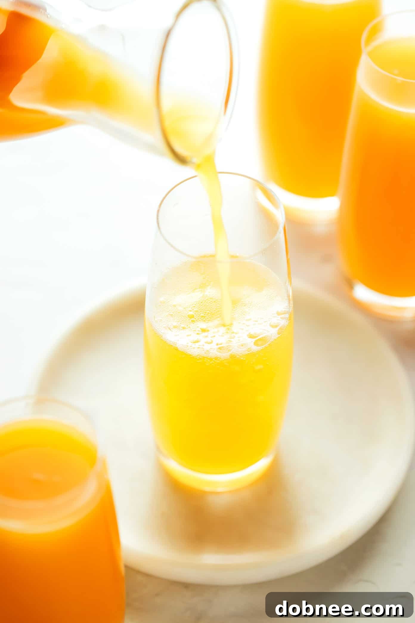 A hand pouring sparkling wine into a champagne flute for a mimosa