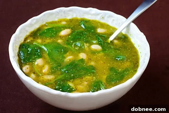 A bowl of vibrant White Bean, Spinach & Pesto Soup, garnished with fresh basil leaves and a sprinkle of Parmesan cheese, ready to be enjoyed.