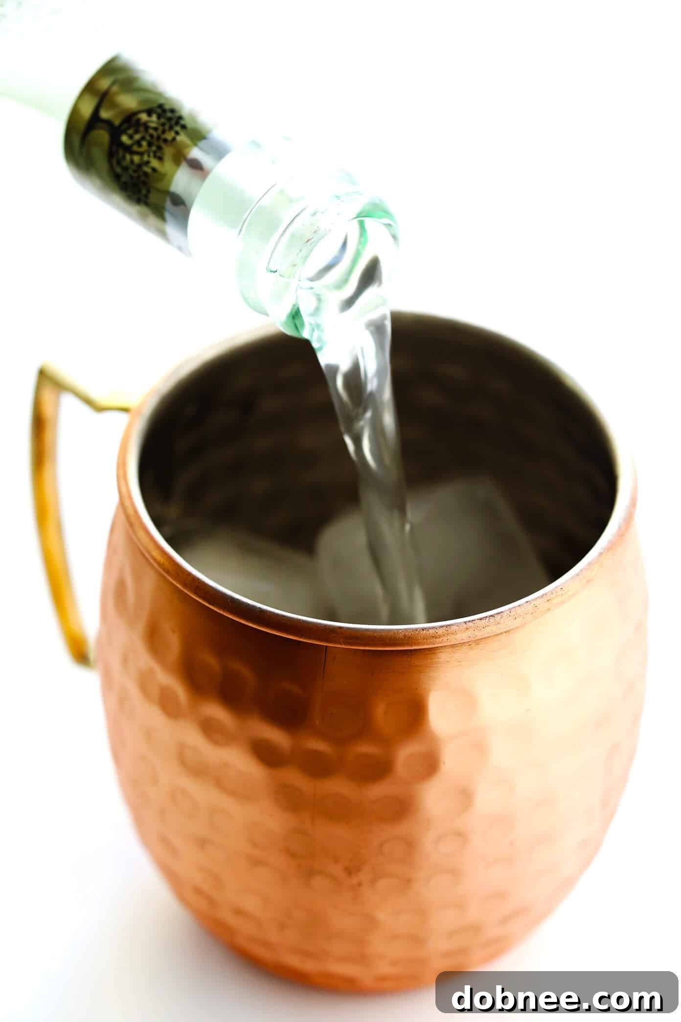 Hands pouring ginger beer into a copper mug with vodka, lime, and ice to make a Moscow Mule.
