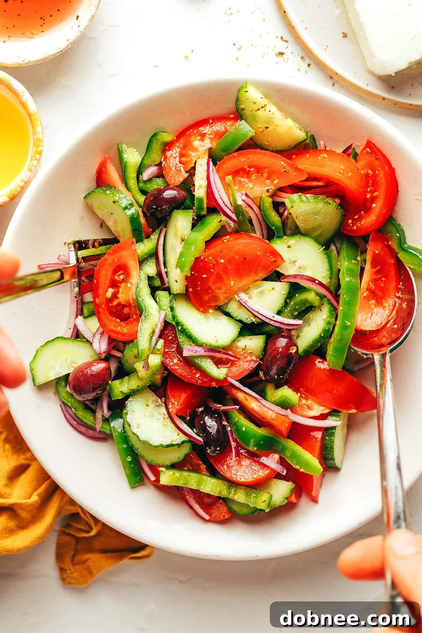 Hand drizzling olive oil over a bowl of Greek Salad ingredients