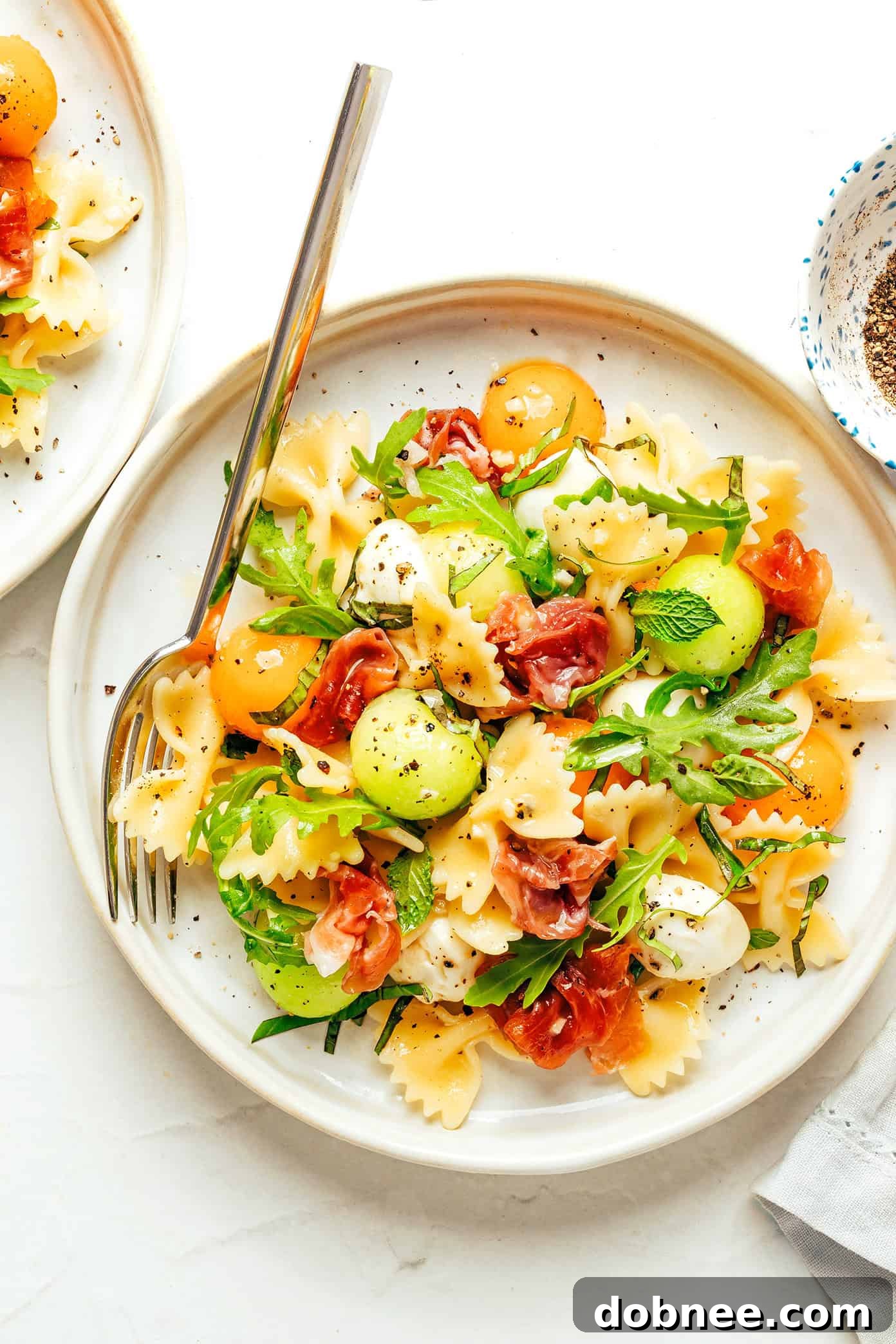 Melon Prosciutto Pasta Delight 2 A vibrant Prosciutto Melon Pasta Salad in a large serving bowl, featuring colorful farfalle pasta, green arugula, pink prosciutto, and orange melon balls.