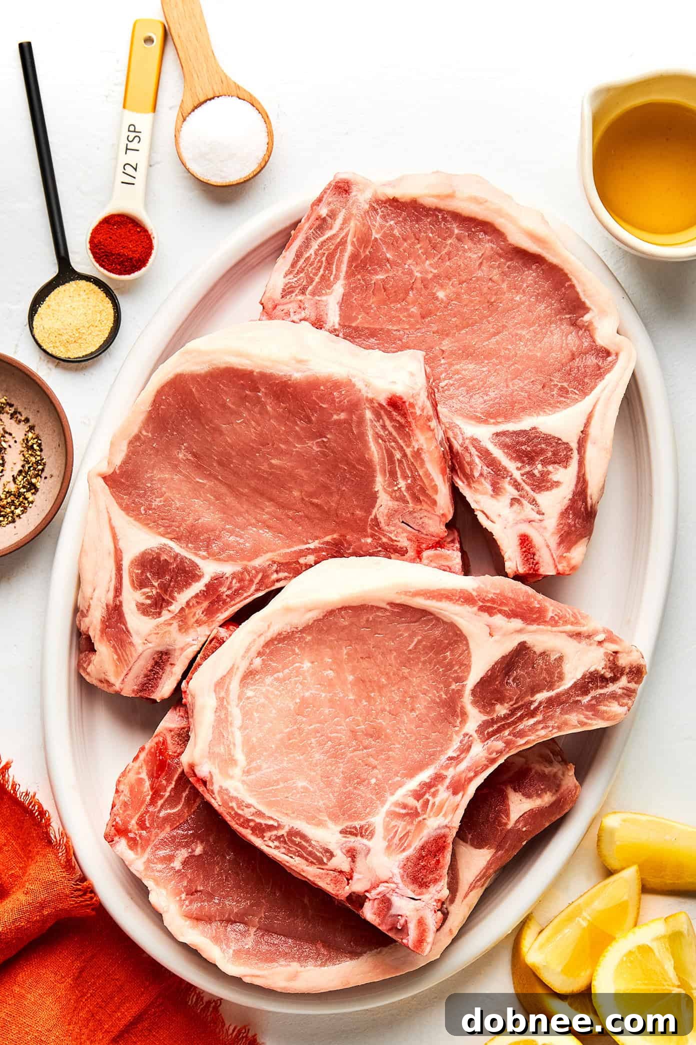 Four raw, thick-cut pork chops seasoned with spices on a cutting board.