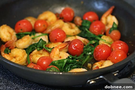 Plate of cooked sautéed shrimp with spinach and tomatoes, with a fork ready to enjoy.
