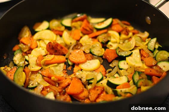 Sweet potatoes, zucchini, and yellow onion simmering and browning in a large skillet with olive oil, creating a fragrant base for the hash.