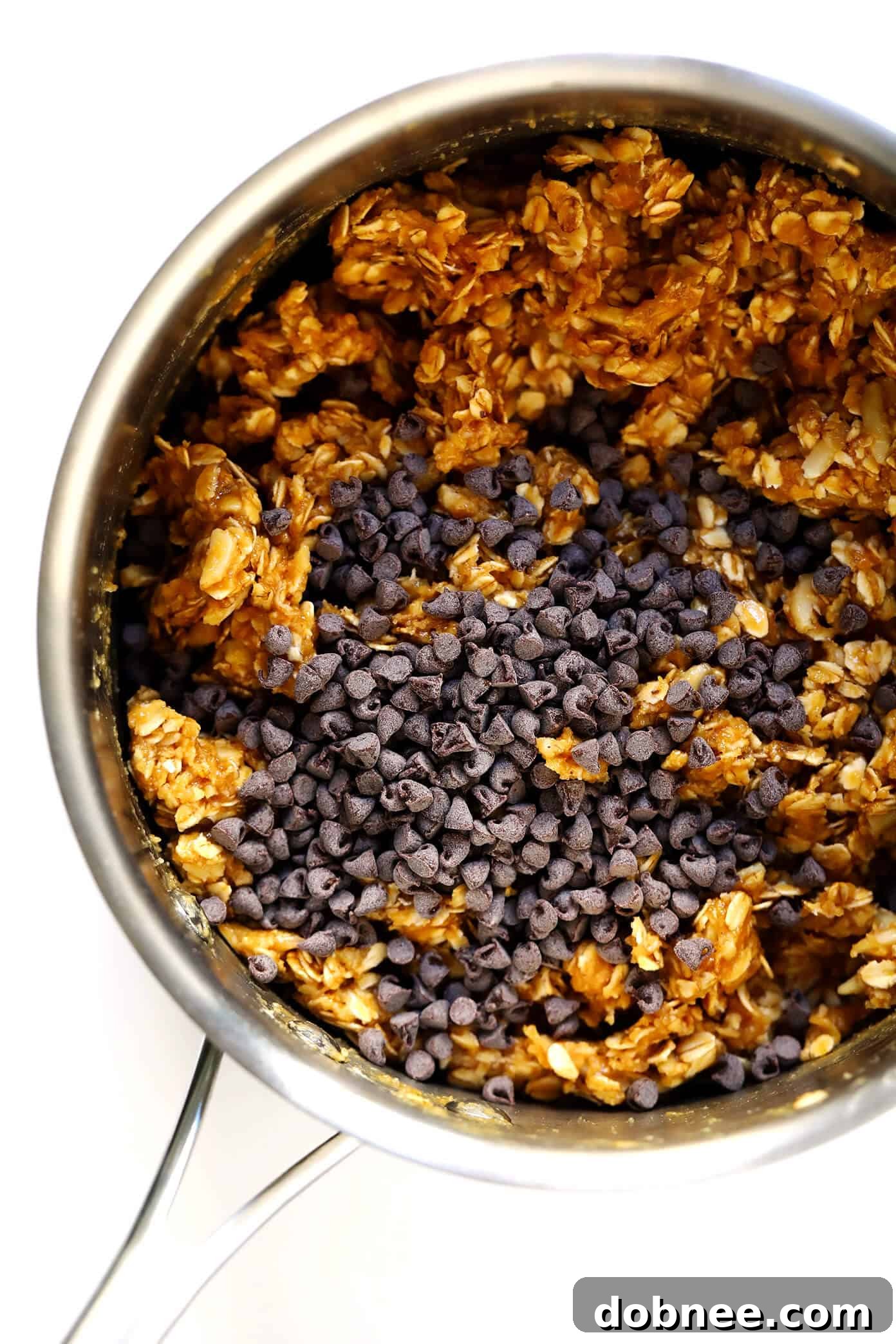 Hands pressing the granola bar mixture firmly into a parchment-lined baking pan.
