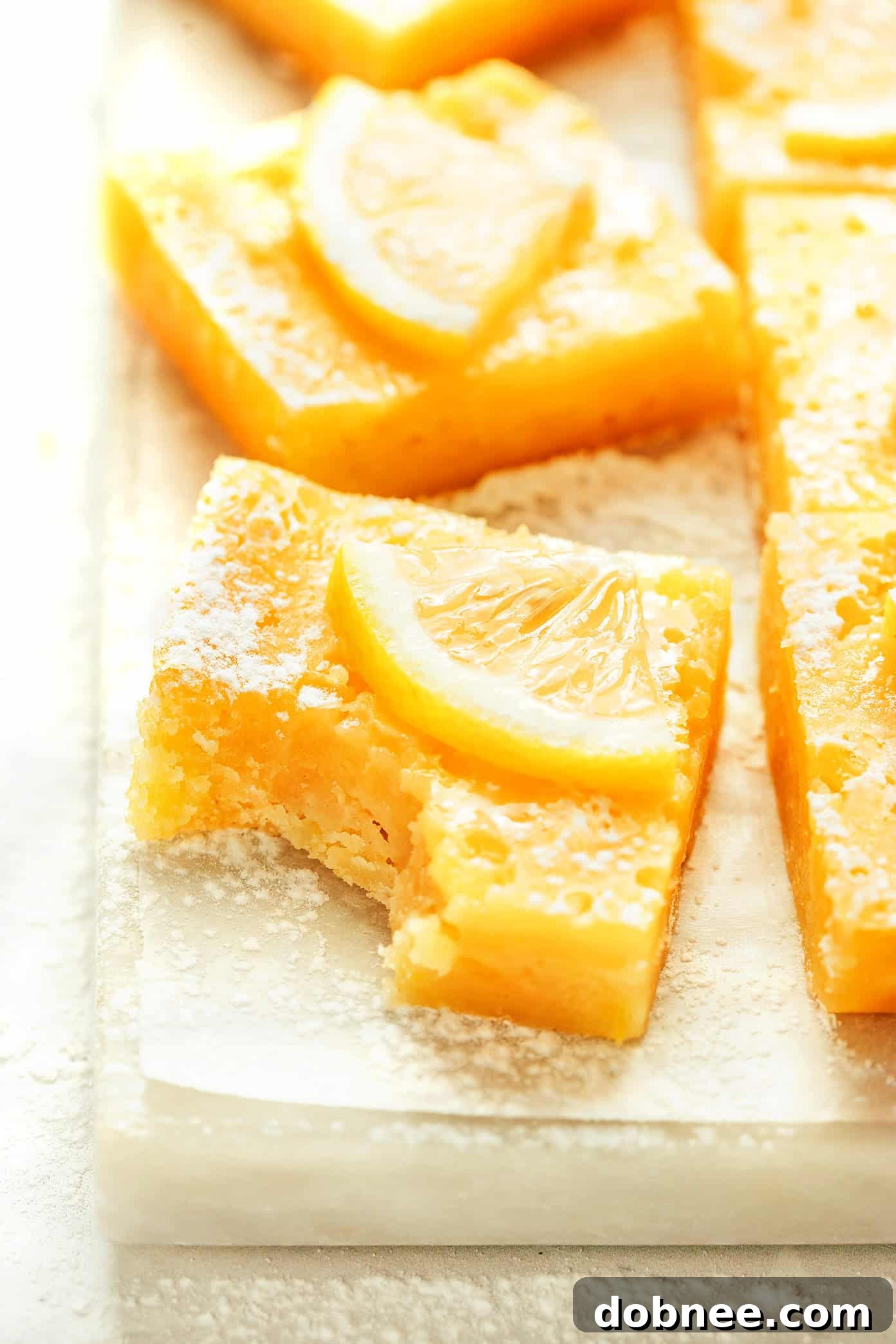 A stack of perfectly cut lemon bars with a dusting of powdered sugar on a white plate.